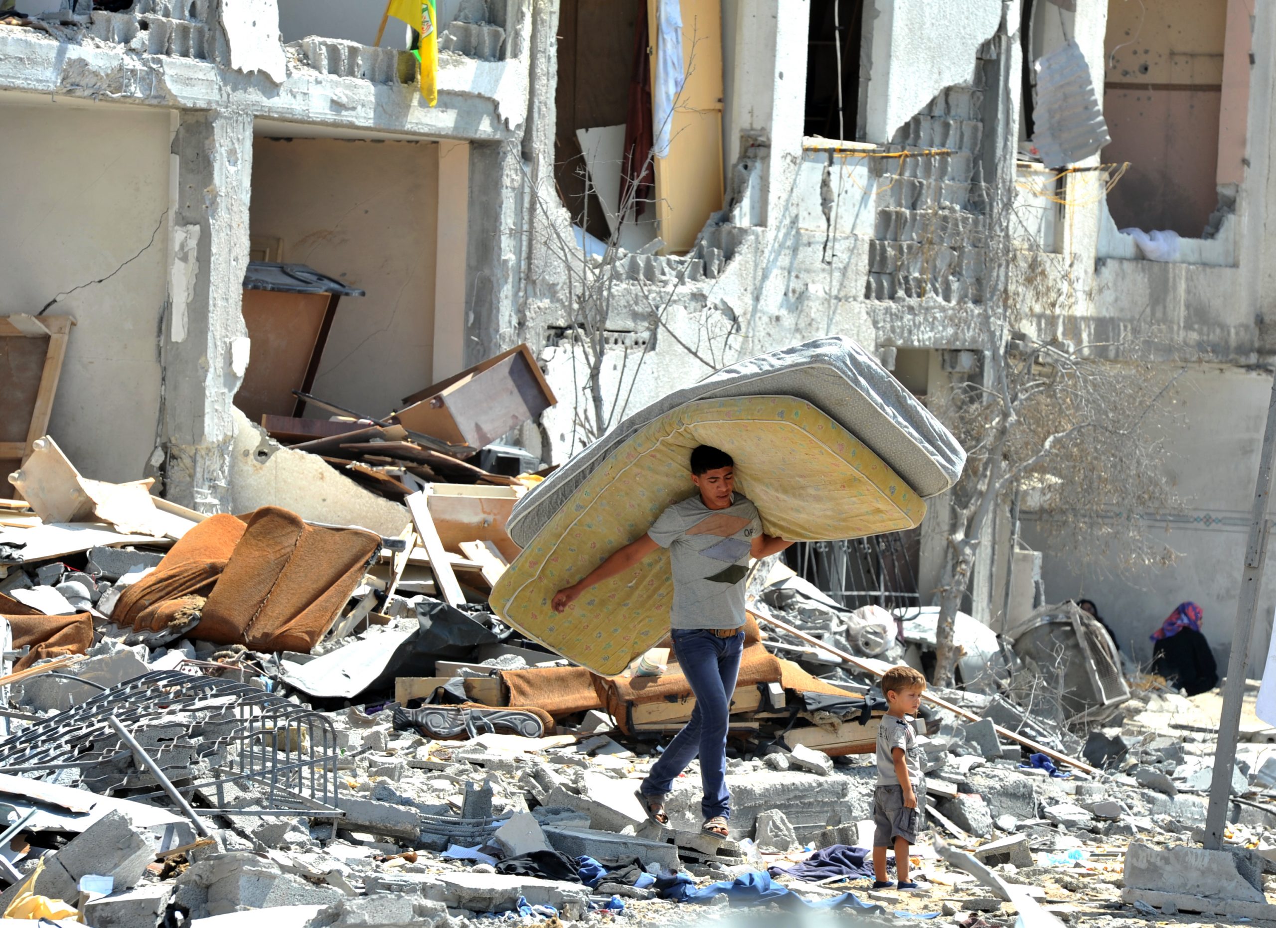 A young man carries a mattress over his head through a ruined Gaza neighbourhood in 2014.