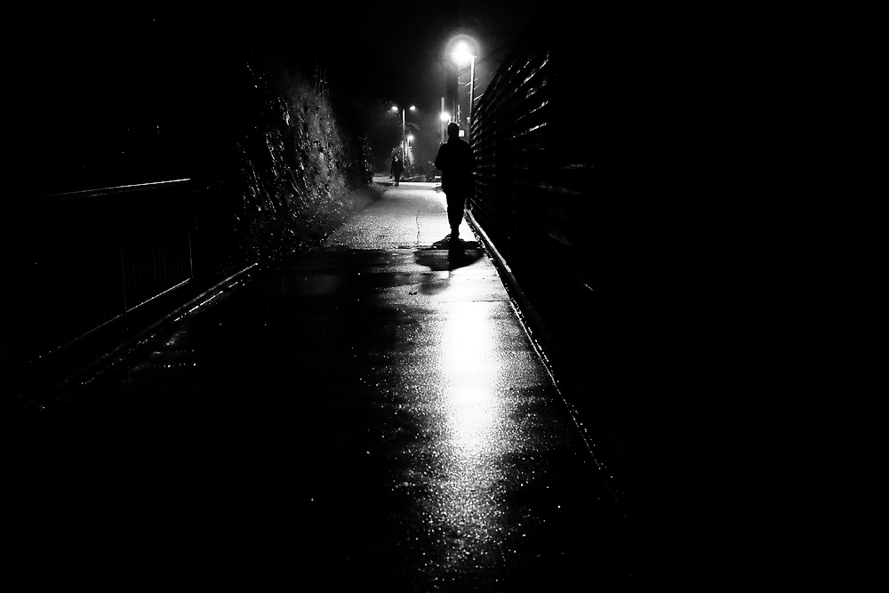 A lone figure walking in a dark street under the light of a street lamp