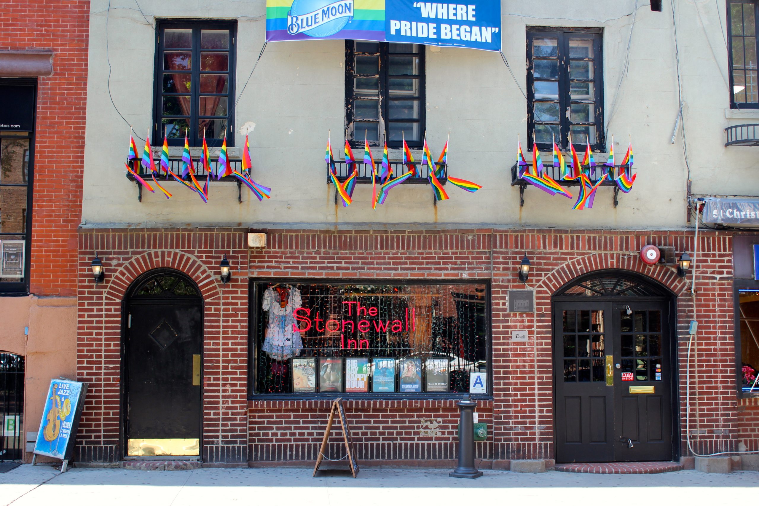 An image of The Stonewall Inn, a brick building in New York. There are pride flags hanging from the first floor windows