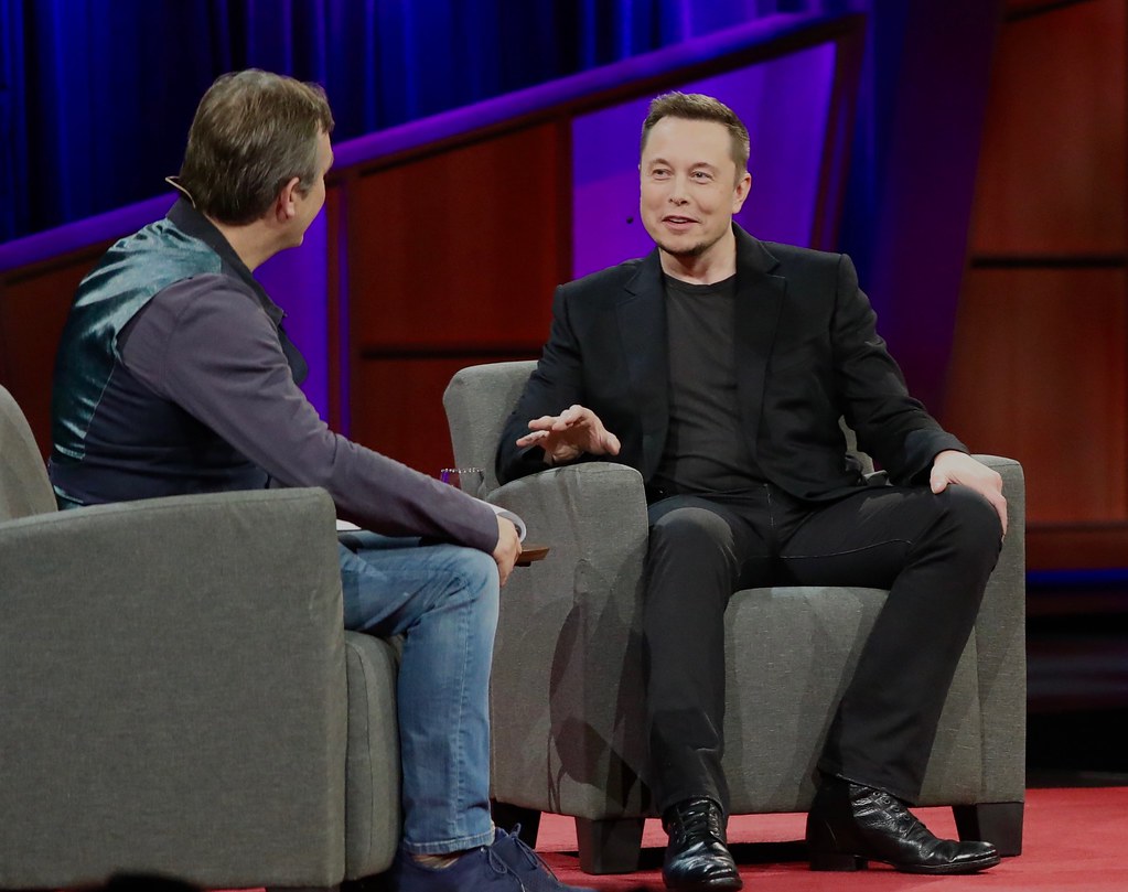Elon Musk sitting in an armchair on a stage.