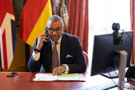 Home Secretary James Cleverly sitting at a desk with a phone to his ear