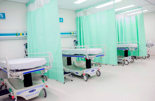 A line of hospital beds with mint coloured privacy curtains separating them.
