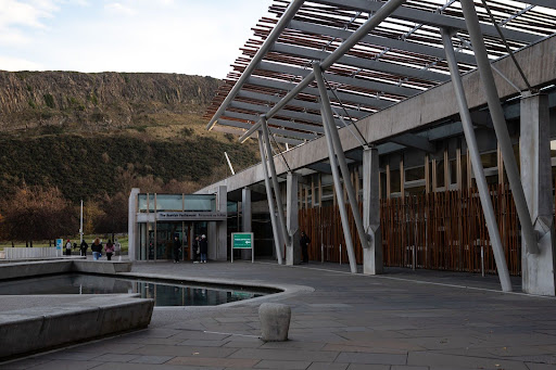 An image of Scottish Parliament with the Salisbury Crags in the background.