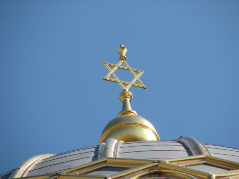 A golden Star of David on top of a domed synagogue roof against a clear blue sky.